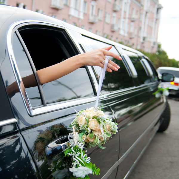 bride holding out her arm with flowers from a limo